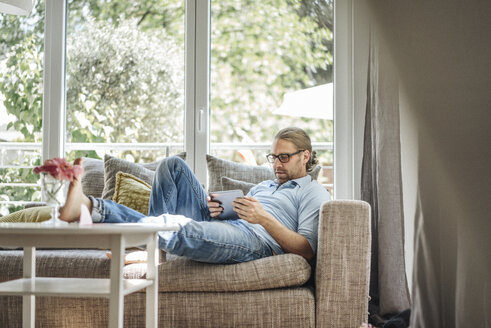 Mann entspannt auf Couch mit Tablet - JOSF00600