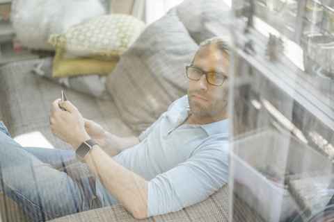 Mann entspannt sich auf der Couch und benutzt ein Mobiltelefon, lizenzfreies Stockfoto