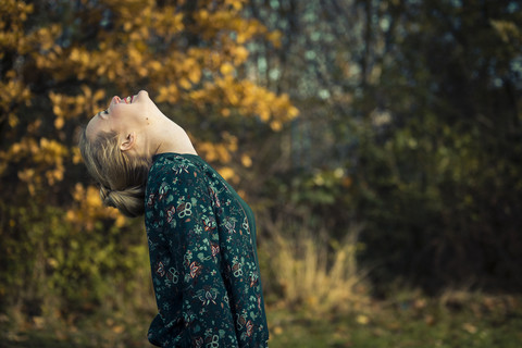 Blonde junge Frau steht mit zurückgelegtem Kopf in einem herbstlichen Wald, lizenzfreies Stockfoto