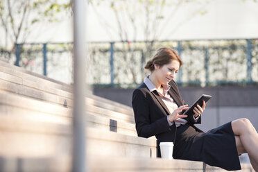 Businesswoman sitting on stairs using tablet - WESTF22589