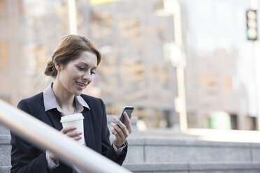 Smiling businesswoman holding cell phone and takeaway coffee - WESTF22593