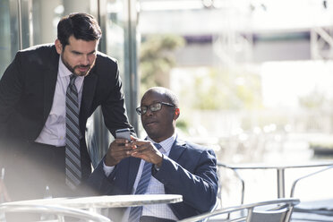 Two businessmen at outdoor cafe looking at cell phone - WESTF22595