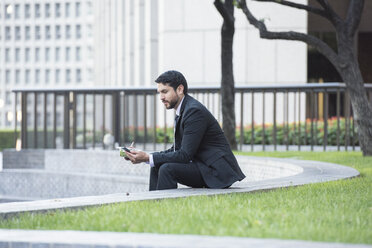 Geschäftsmann, der auf einer Außentreppe sitzt, zu Mittag isst und ein Mobiltelefon benutzt - WESTF22603