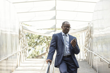 Businessman checking cell phone on stairs - WESTF22627