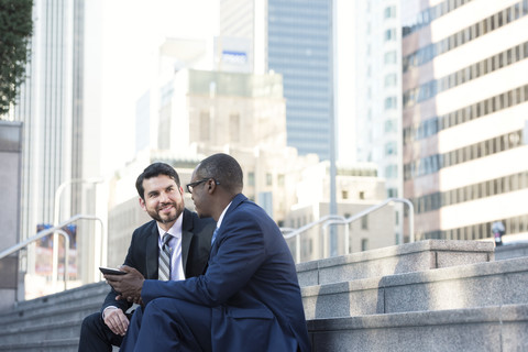 Zwei Geschäftsleute sitzen auf einer Treppe und unterhalten sich über ein Tablet, lizenzfreies Stockfoto