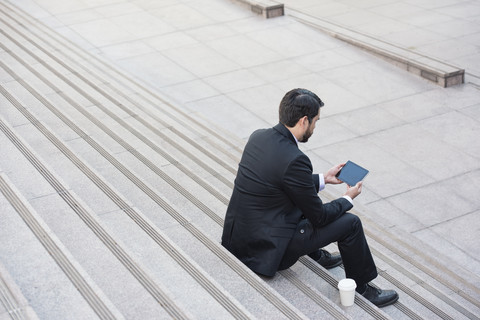 Geschäftsmann sitzt auf einer Treppe mit Tablet und Kaffee zum Mitnehmen, lizenzfreies Stockfoto