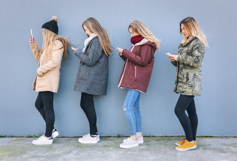 Four young women standing in a row using their cell phones - MGOF02922