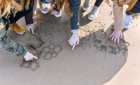 Vier Freunde zeichnen im nassen Sand am Strand, Teilansicht, lizenzfreies Stockfoto