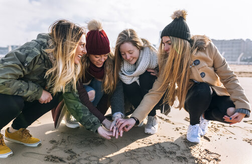 Vier Freunde reichen sich am Strand die Hände - MGOF02928