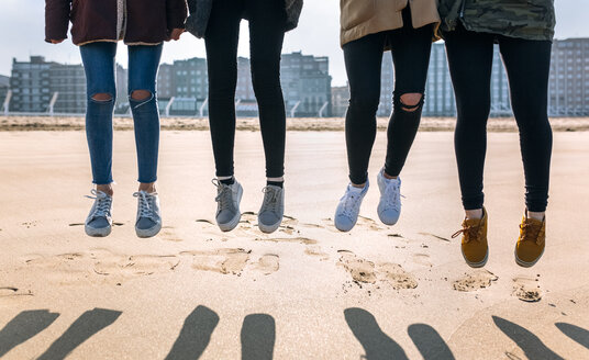 Beine von vier Freunden, die am Strand in die Luft springen - MGOF02930