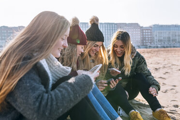 Four friends sitting on the beach text messaging - MGOF02932