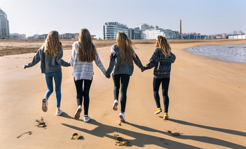 Spanien, Gijon, Rückenansicht von vier Freunden, die Hand in Hand am Strand laufen, lizenzfreies Stockfoto