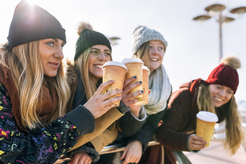 Vier Freunde stoßen im Winter mit Kaffee zum Mitnehmen an, lizenzfreies Stockfoto