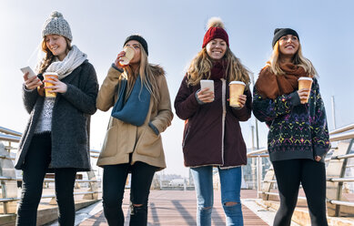 Four friends with coffee to go and cell phones walking on a bridge in winter - MGOF02949
