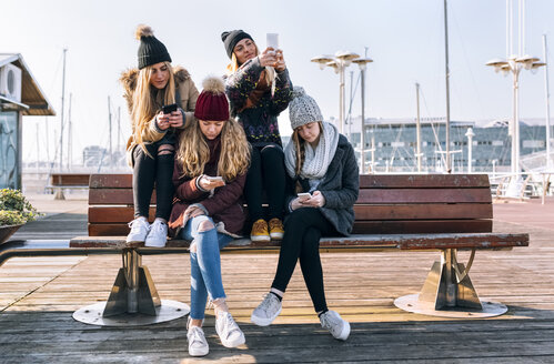 Vier junge Frauen sitzen auf einer Bank und benutzen ihre Handys - MGOF02951
