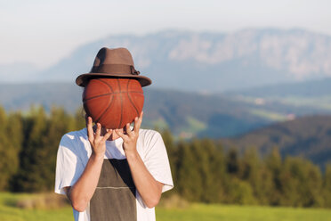 Österreich, Mondsee, Mondseeberg, junger Mann verdeckt sein Gesicht mit einem Basketball - WVF00845