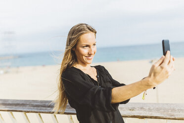 Lächelnde junge Frau macht ein Selfie am Strand - GIOF01820