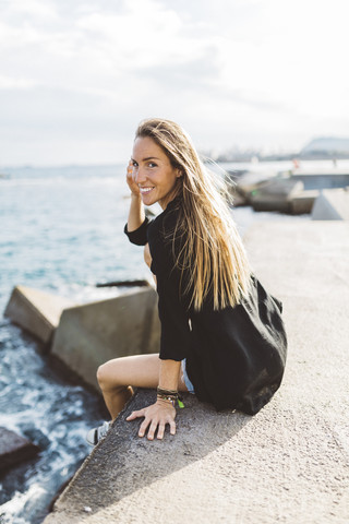 Portrait of smiling young woman sitting at the seafront stock photo