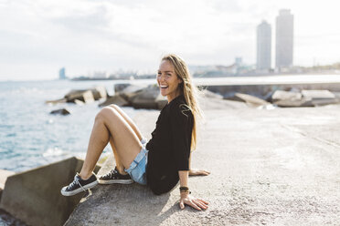 Porträt einer glücklichen jungen Frau, die an der Strandpromenade sitzt - GIOF01829
