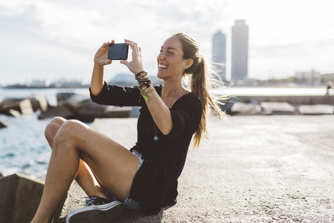 Glückliche junge Frau schaut auf ihr Handy an der Strandpromenade, lizenzfreies Stockfoto