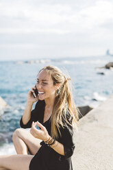 Glückliche junge Frau an der Strandpromenade mit Handy - GIOF01836