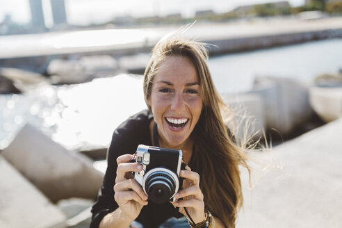 Porträt einer glücklichen jungen Frau mit altmodischer Kamera an der Strandpromenade - GIOF01840