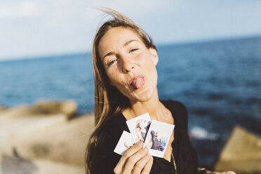 Freche junge Frau, die Sofortfotos von sich an der Strandpromenade zeigt - GIOF01847