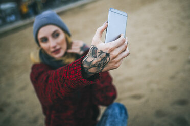 Nahaufnahme einer tätowierten Frauenhand, die ein Selfie am Strand macht. - KIJF01191