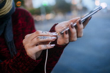 Nahaufnahme einer tätowierten Frauenhand, die einen Miniklinkenstecker an ein Smartphone anschließt - KIJF01203