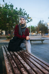 Young woman sitting on a bench listening to music - KIJF01206