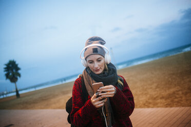 Young woman listening to music on a smartphone on the beach at dusk - KIJF01208