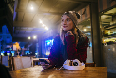 Junge Frau mit Mobiltelefon auf der Terrasse einer Bar sitzend - KIJF01209