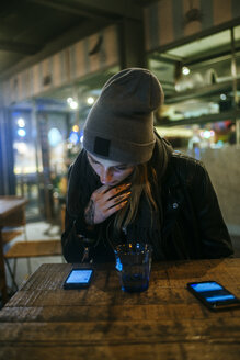 Junge Frau sitzt auf der Terrasse einer Bar und schaut auf ihr Handy - KIJF01210