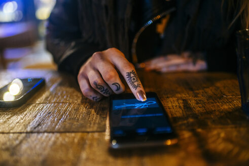 Nahaufnahme der Hände einer tätowierten Frau, die auf einem Smartphone unterschreibt - KIJF01211