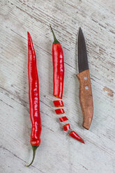 Ganze und geschnittene rote Chilischoten und ein Küchenmesser auf Holz - JUNF00830