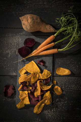 Vegetable chips made of carrots, sweet patatoes and beetroot on dark wood stock photo