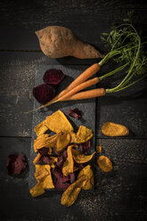 Vegetable chips made of carrots, sweet patatoes and beetroot on dark wood - MAEF12134