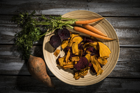 Vegetable chips made of carrots, sweet patatoes and beetroot on plate and dark wood stock photo