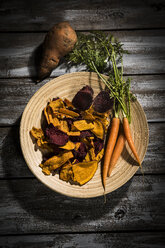 Vegetable chips made of carrots, sweet patatoes and beetroot on plate and dark wood - MAEF12137