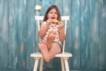 Füße eines kleinen Mädchens, das auf einem Stuhl sitzt und einen Zitroneneislutscher isst - RTBF00653