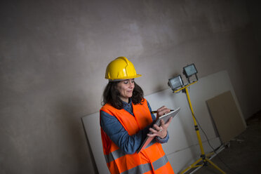 Frau mit Schutzhelm und Warnweste auf einer Baustelle schreibt in ein Notizbuch - KIJF01213