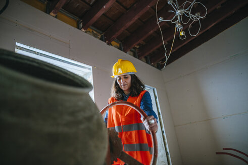 Woman working with a concrete mixer on construction site - KIJF01216