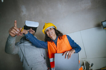 Frau auf Baustelle zeigt einem Mann mit Virtual-Reality-Brille das Haus - KIJF01217