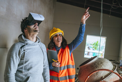 Frau auf Baustelle zeigt einem Mann mit Virtual-Reality-Brille das Haus - KIJF01218