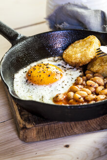 Spiegelei, Baked Beans und Rösti in der Pfanne auf dem Holzbrett - SBDF03149