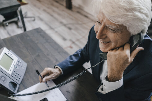 Lächelnder älterer Geschäftsmann am Telefon in seinem Büro - KNSF01011