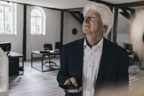 Smiling senior businessman with cell phone in his office - KNSF01012