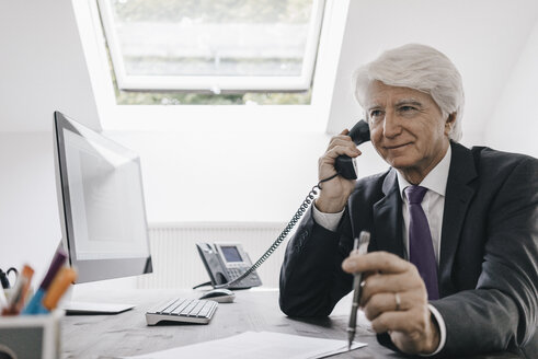 Ein älterer Geschäftsmann telefoniert an seinem Schreibtisch - KNSF01021