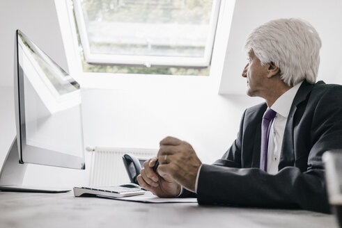 Senior businessman sitting at desk in his office looking through window - KNSF01022