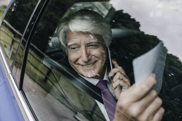 Lächelnder älterer Geschäftsmann mit Dokumenten am Telefon in einem Auto - KNSF01029